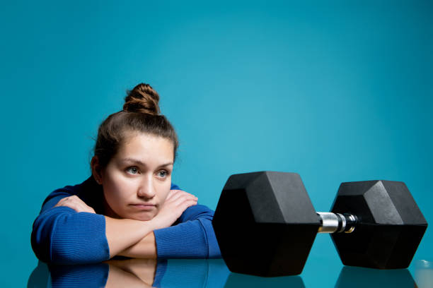 the girl put her head in her hands and looks at the dumbbell that lies in front of her the girl put her head in her hands and looks at the big dumbbell that lies in front of her wasting time photos stock pictures, royalty-free photos & images