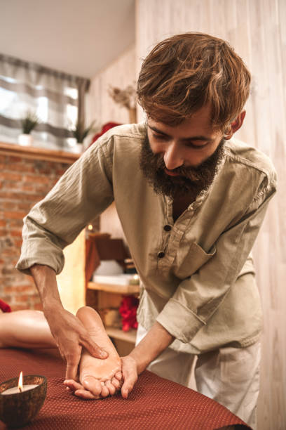 médecine alternative. femme de guérison de thérapeute faisant le massage ayurvédique avec la bougie d'arôme sur le pied pressant dans le plan rapproché pensif moyen - ayurveda massaging aromatherapy chakra photos et images de collection