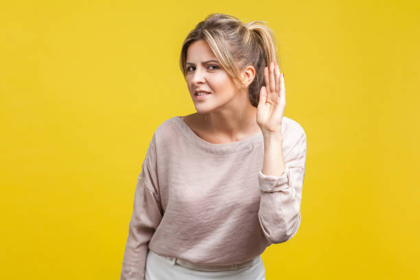 what? i can't hear you! portrait of young woman with fair hair in casual beige blouse, isolated on yellow background - spy secrecy top secret mystery imagens e fotografias de stock