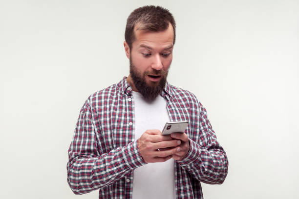 istock Portrait of surprised bearded man using smartphone looking amazed shocked about message. white background 1194574037
