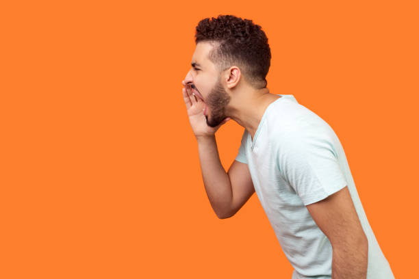 Attention! Side view of angry brunette man screaming loud with wide open mouth. indoor studio shot isolated on orange background stock photo