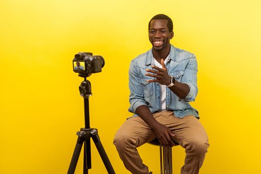 Live blog. Portrait of positive friendly happy man smiling at his professional dslr camera. isolated on yellow background