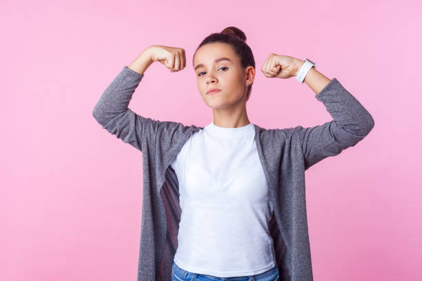 Portrait of self-confident teenage girl raising hands showing power, feeling independent. isolated on pink background Portrait of self-confident teenage girl with bun hairstyle in casual clothes raising hands showing power, feeling independent strong with proud look. indoor studio shot isolated on pink background 14 15 years photos stock pictures, royalty-free photos & images