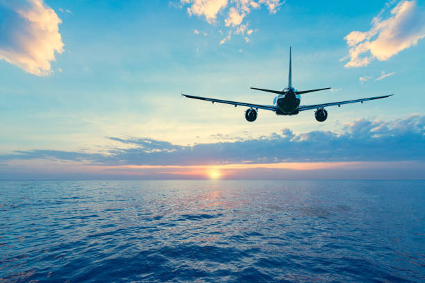 Flying of the passenger plane above the sea surface. Flying of the passenger plane above the sea surface at sunset time. planes flying overhead stock pictures, royalty-free photos & images