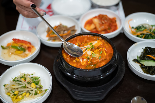 Asian woman enjoying Korean kimchi soup and tableful of side dishes