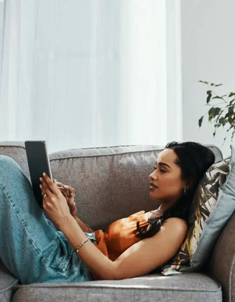Shot of a young woman using a digital tablet on the sofa at home