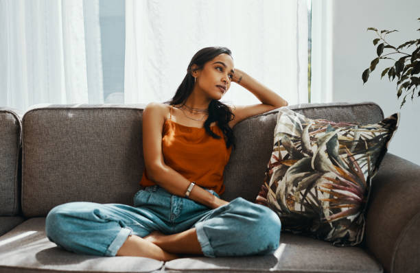 Take a day off to get your thoughts in order Shot of a young woman looking thoughtful while relaxing on the sofa at home cross legged stock pictures, royalty-free photos & images