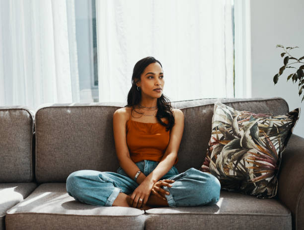 Alone with her thoughts to keep her company Shot of a young woman looking thoughtful while relaxing on the sofa at home menstruation stock pictures, royalty-free photos & images