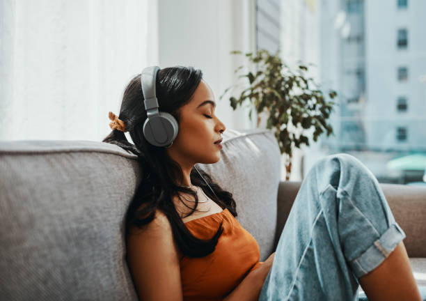 Nothing evokes memory like music Shot of a young woman using headphones while relaxing on the sofa at home eyes closed stock pictures, royalty-free photos & images