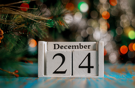 December 24 th on wooden calendar cube with christmas tree lights background. Christmas eve concept