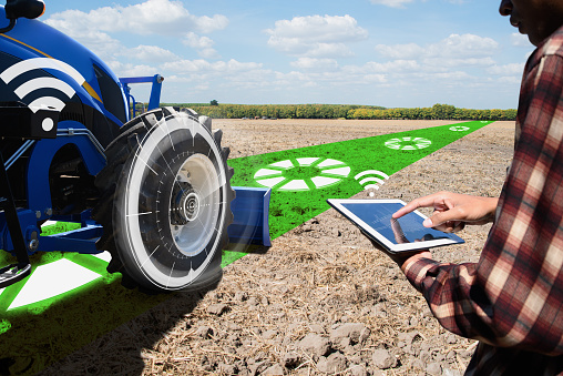 IOT smart industry robot 4.0 agriculture concept.Autonomous tractor working in farm.Smart farming and digital transformation in agriculture.farmer with tablet controls autonomous tractor in farm.