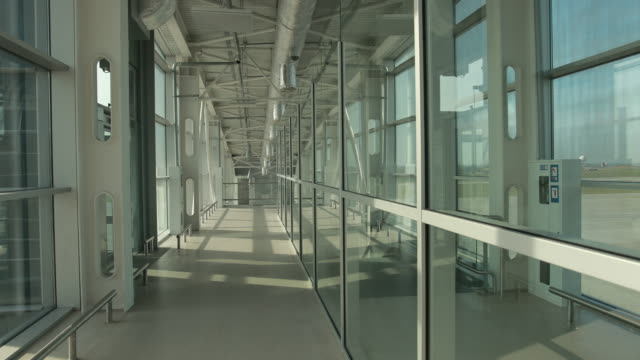 Stylish glass corridor in airport terminal to runway with planes.