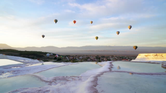 Hot air balloons in travertine pools limestone terraces at sunrise in Pamukkale, Denizli