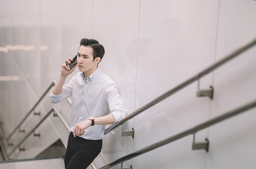 an asian chinese business casual man talking over the phone at the staircase of right rail staion