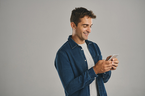 Studio shot of a young man using a cellphone against a grey background