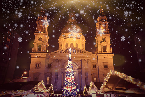 Budapest christmas market with christmas tree, market stalls and St. Stephen's Basilica with added snowflakes; advent basilica christmas market is one of Europe's most beautiful Christmas markets.