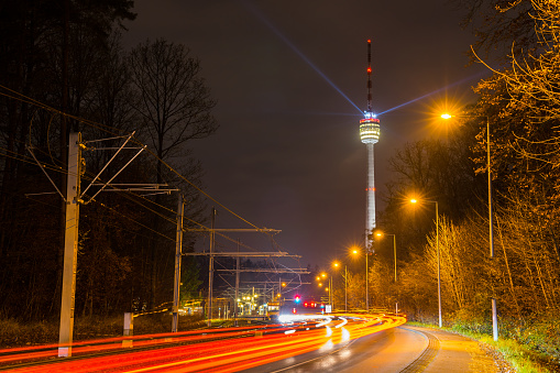 Germany, Dark night sky over famous stuttgart television tower or tv tower building behind busy street of traffic and trams in forest of the city