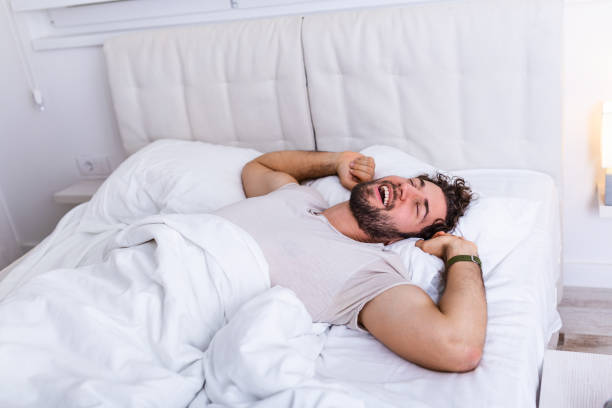istock Young man sleeping waking up and stretching in his bed. people, bedtime and rest concept - man lying in bed at home, It's time to wake up 1194632033