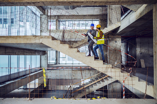 Trabajador de la construcción y arquitecto principal subiendo las escaleras y hablando de avances en la construcción de un nuevo edificio. photo