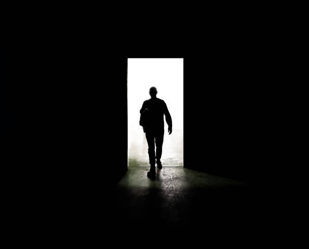 Mysterious man walking through door in between darkness and light stock photo