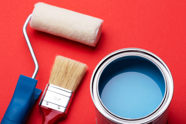 Can of blue paint, paint roller and brushe on red.