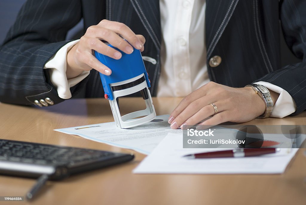 A businesswoman notarizing a document with a stamp Young businesswoman (or notary public) sitting at the desk in office and stamping document Shorthand Stock Photo