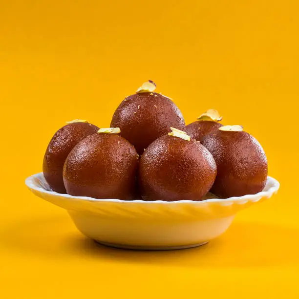 Indian Dessert or Sweet Dish : Gulab Jamun in white bowl on yellow background