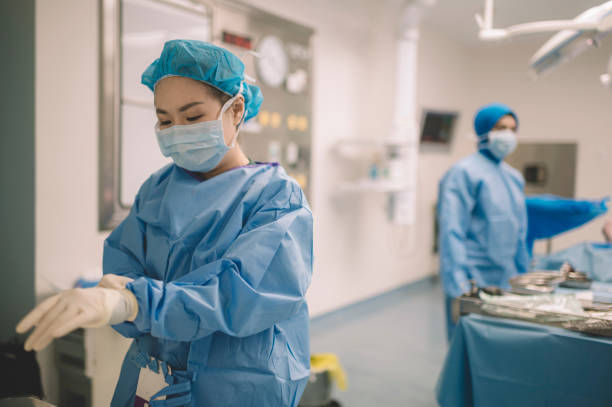 un médico cirujano chino asiático está usando guantes quirúrgicos antes de la cirugía en el quirófano - hair net nurse scrubs asian ethnicity fotografías e imágenes de stock