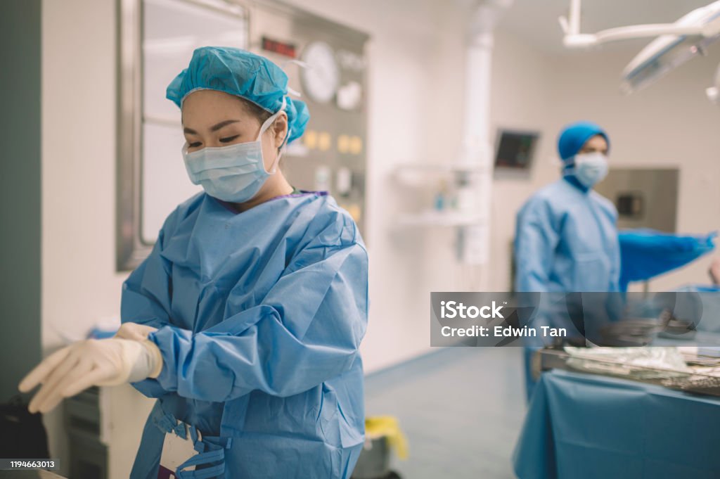 an asian chinese female surgeon doctor is wearing surgical gloves before the surgery in operating room Nurse Stock Photo