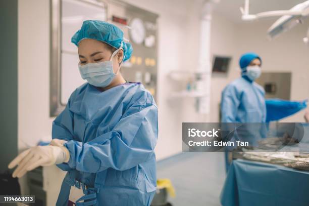 An Asian Chinese Female Surgeon Doctor Is Wearing Surgical Gloves Before The Surgery In Operating Room Stock Photo - Download Image Now