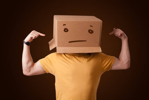 istock Young man gesturing with a cardboard box on his head with straight face 1194663197