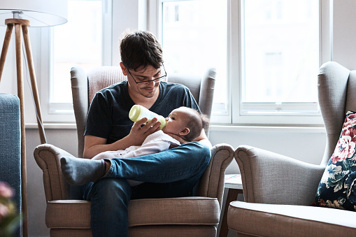 Shot of a happy father feeding and spending time with his infant daughter at home