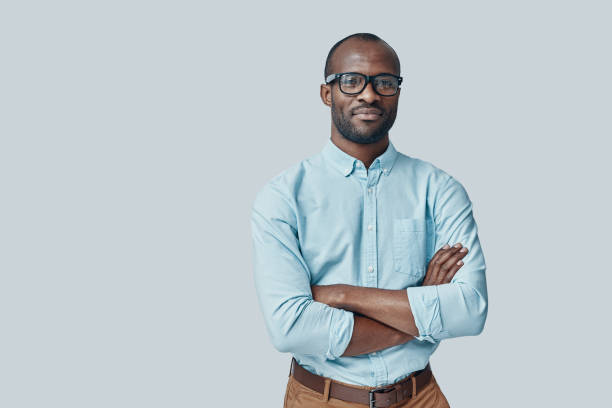 Confident young African man Confident young African man looking at camera and smiling while standing against grey background black man stock pictures, royalty-free photos & images