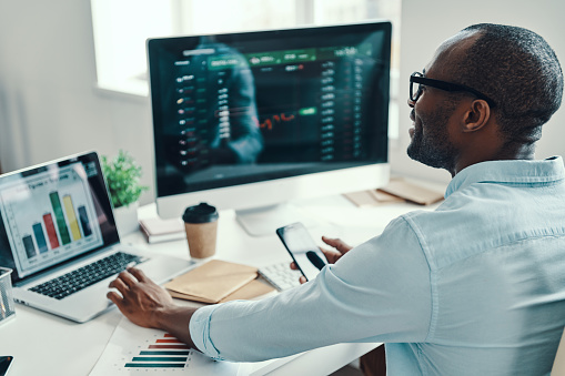 Handsome young African man in shirt using computer and smiling while working in the office