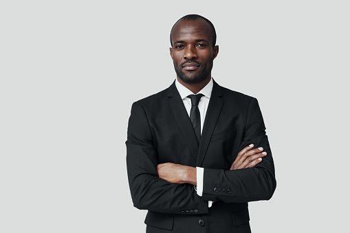Handsome young African man in formalwear looking at camera while standing against grey background