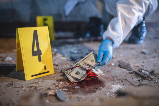 Bloody US Currency Evidence at Urban Crime Scene Close-up of gloved hand picking up bloody US currency evidence marked by yellow number 4 at run-down urban crime scene. bloody money stock pictures, royalty-free photos & images