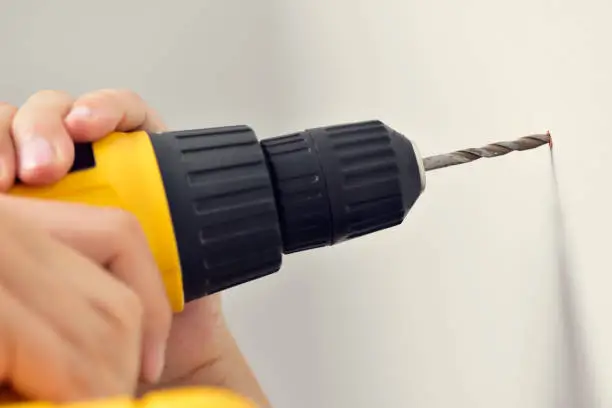 closeup of a young caucasian man making a hole in a wall with a drill