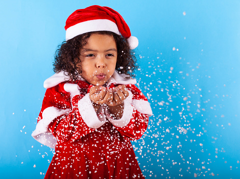 African-American little girl in Santa Claus hat blowing snowflakes