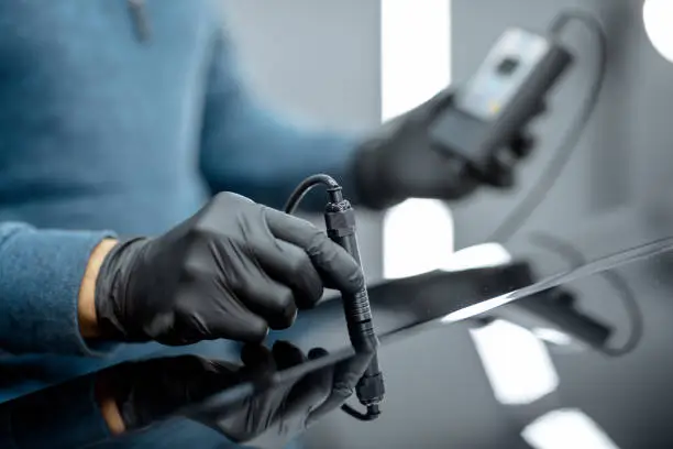 Inspector measuring paint cover thickness of the car body at the vehicle service box, close-up view on hands and professional thickness meter