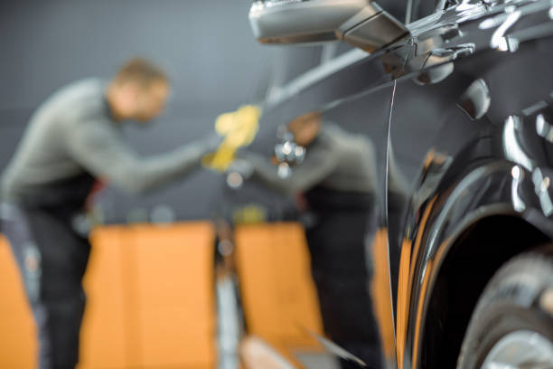 Worker wiping vehicle body with microfiber at the service Car service worker wiping vehicle body with microfiber, examining glossy coating after the polishing procedure. Man blurred on the background car bodywork stock pictures, royalty-free photos & images