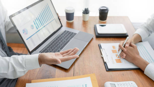 istock Midsection Of Colleagues With Laptop Analyzing Charts On Office Desk 1194691833