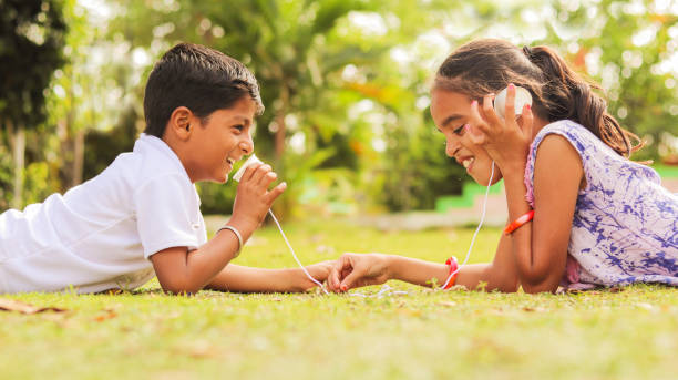 Two children having fun by playing with String Telephone at park during vacation - Concept of socializing by playing outdoor games in the technology driven world