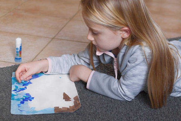 ブ�ロンドの女の子が白い紙に雑誌から形を切り取り、コラージュを作る - glue white education craft ストックフォトと画像