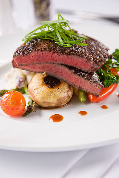 Tender juicy steak with mushrooms and potato bake on white plate and dressed table in restaurant.