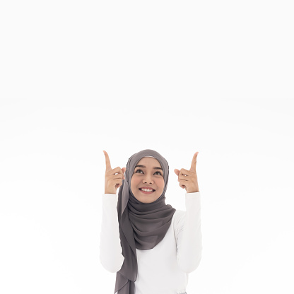 Portrait of good-looking beautiful young asian adult muslim girl wearing white traditional isalamic muslim cloth pointing to blank copy space on white background. Studio shot on white background.