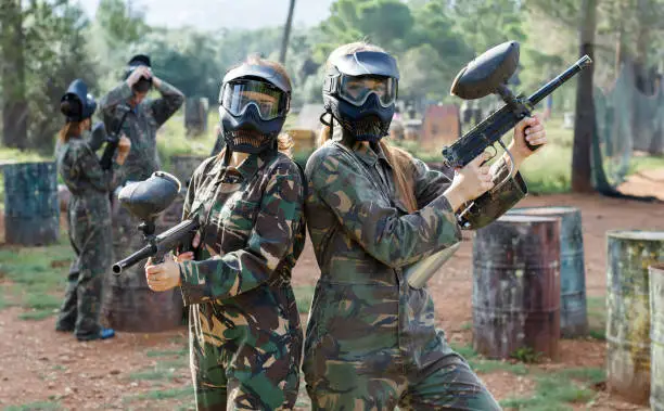 Photo of Portrait of confident female paintball players with marker guns outdoors