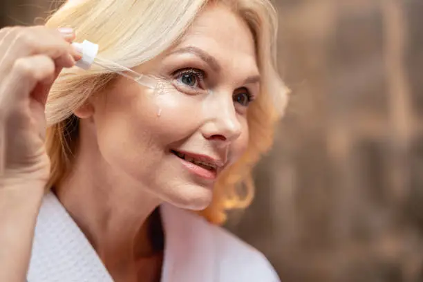 Smiling female applying a face serum with a dropper
