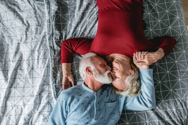 senior couple laying in bed - quilt 60s 70s activity imagens e fotografias de stock