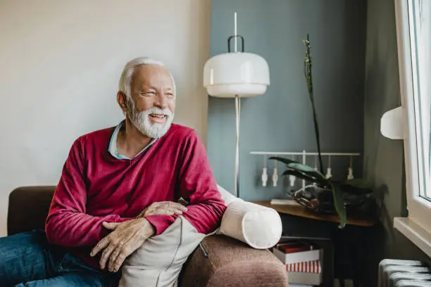 Senior men in a red sweater sitting in a living room at home and looking at window