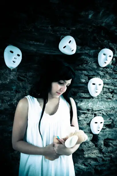 mentally confused woman with cuddly bear in front of a wall with white masks
